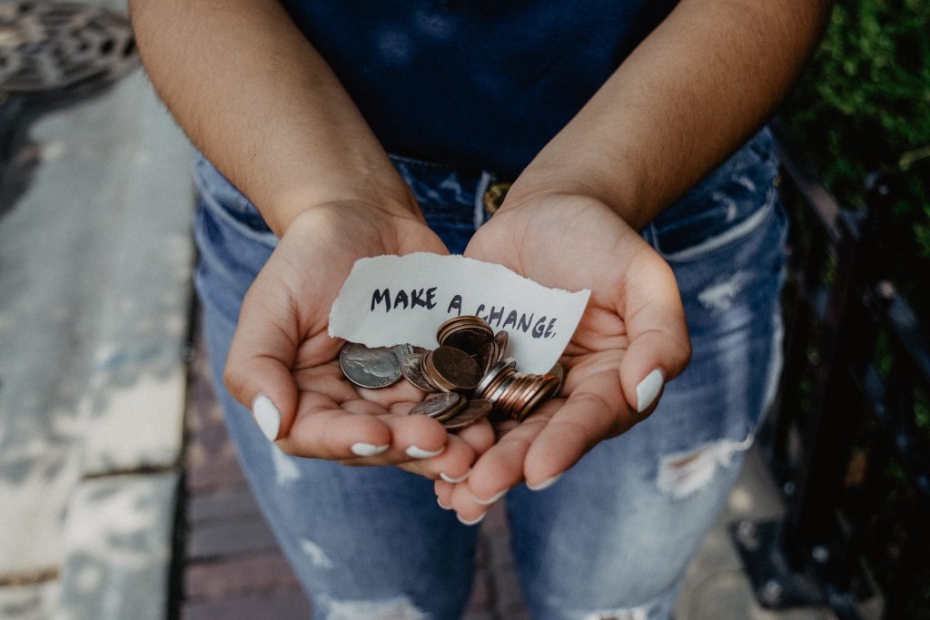 Close up of someone's hands cupped together holding some coins and a piece of paper that says make a change