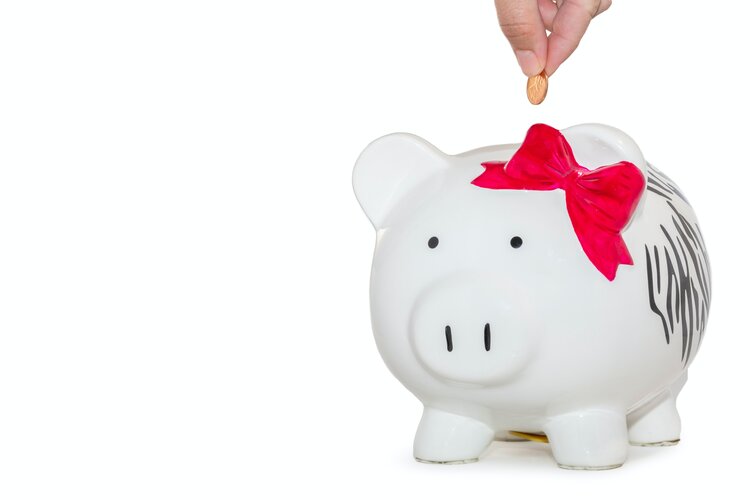 White piggy bank with red bow on ear and someone dropping a coin into it