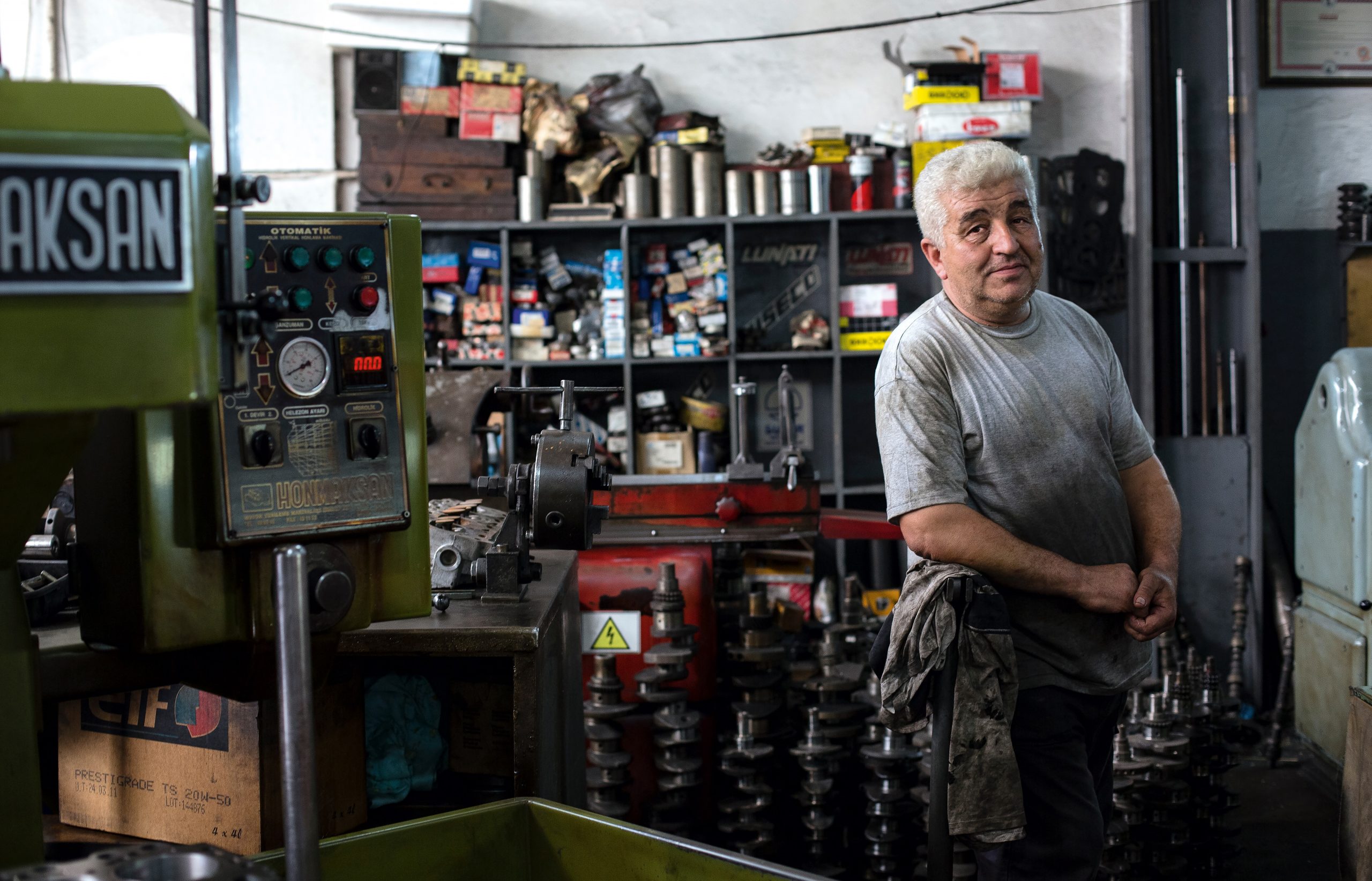 An older gentleman posed inside his business with a bunch of tools and shelving