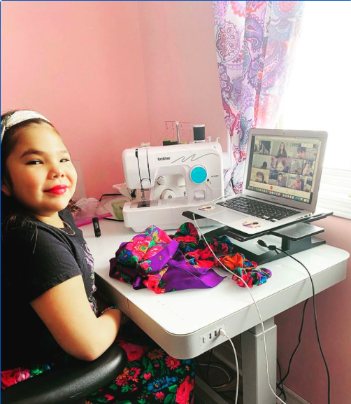 Photo of Mya the founder of Kokom Scrunchies sitting at a desk with her laptop, fabric and sewing machine