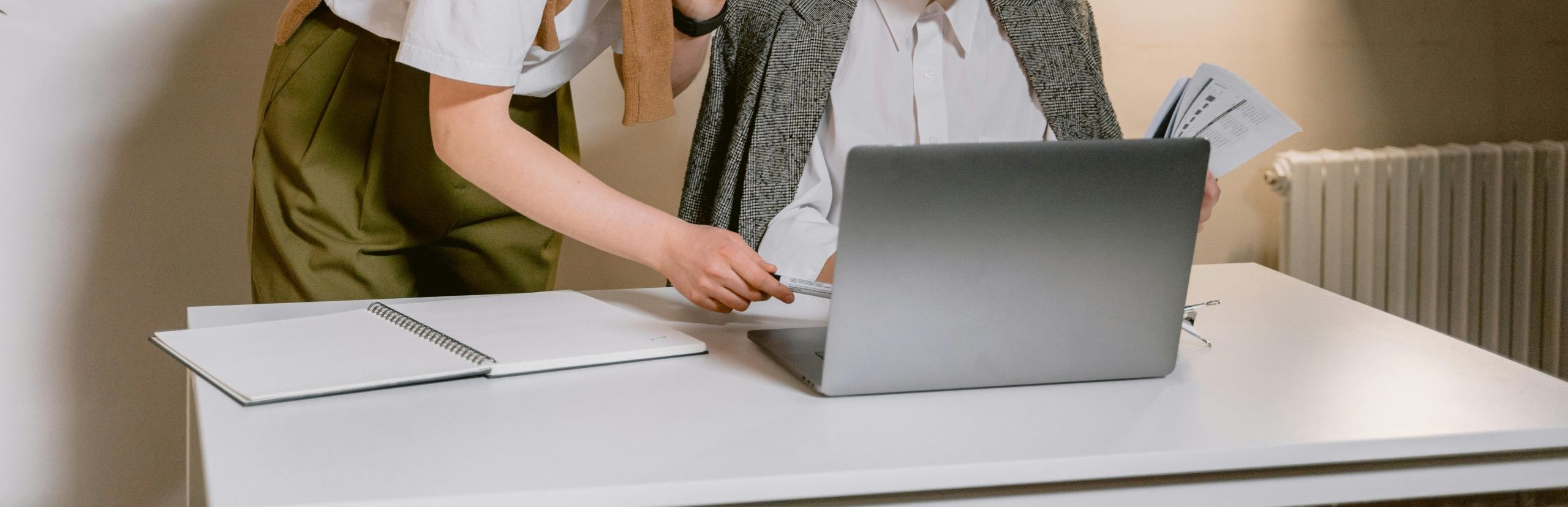 Two women working together and hovered over a laptop at a desk